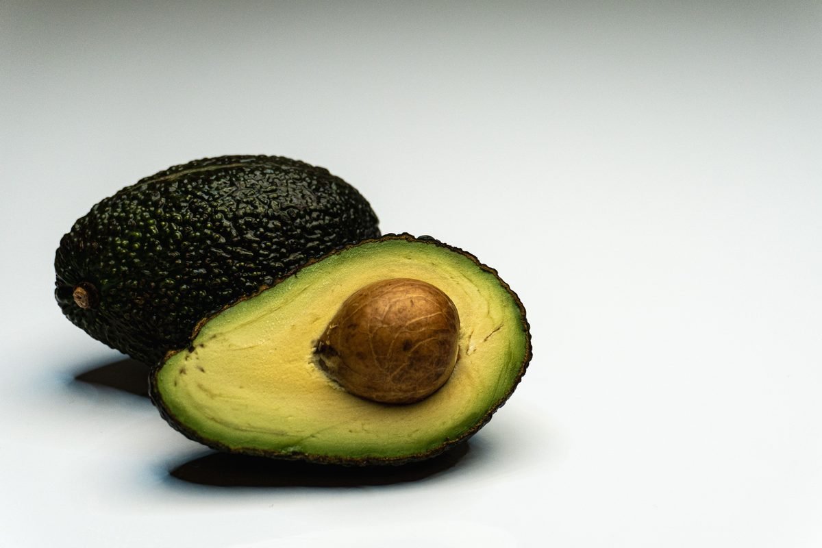 A whole avocado beside a halved avocado showing the pit