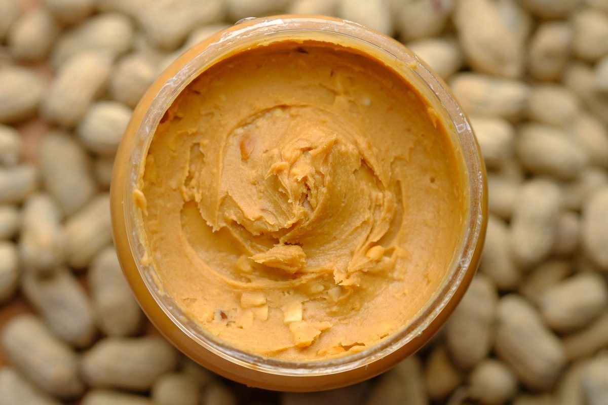 An open jar of peanut butter surrounded by shelled peanuts